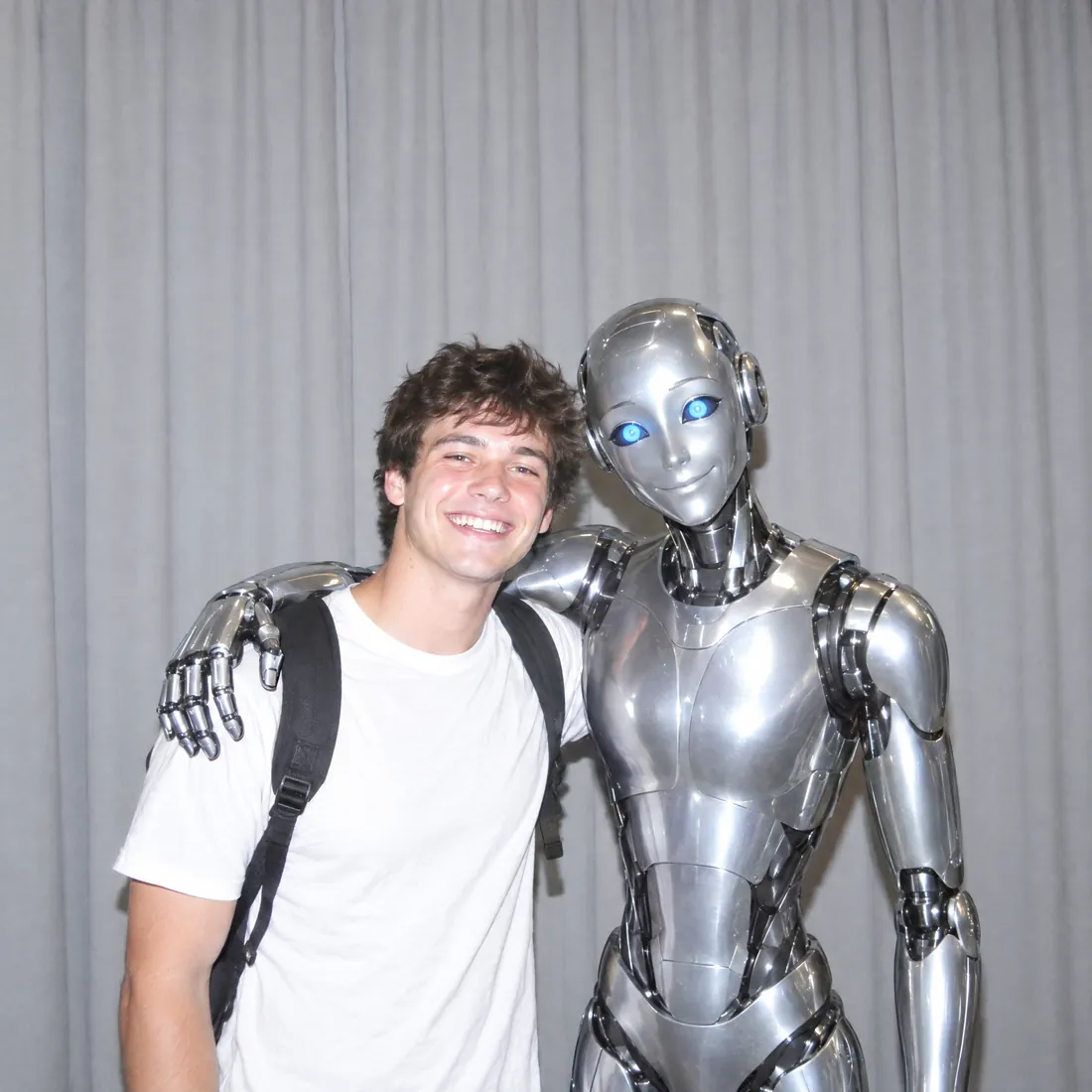 A smiling young man hugging a friendly chrome robot like a best friend
