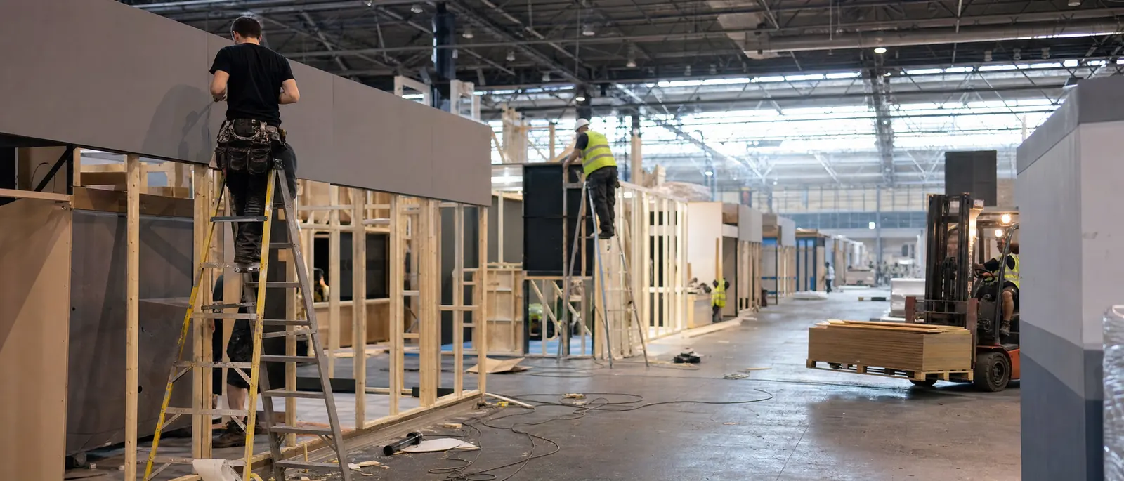 An exhibition hall on build-up day, stands half built, crews on ladders