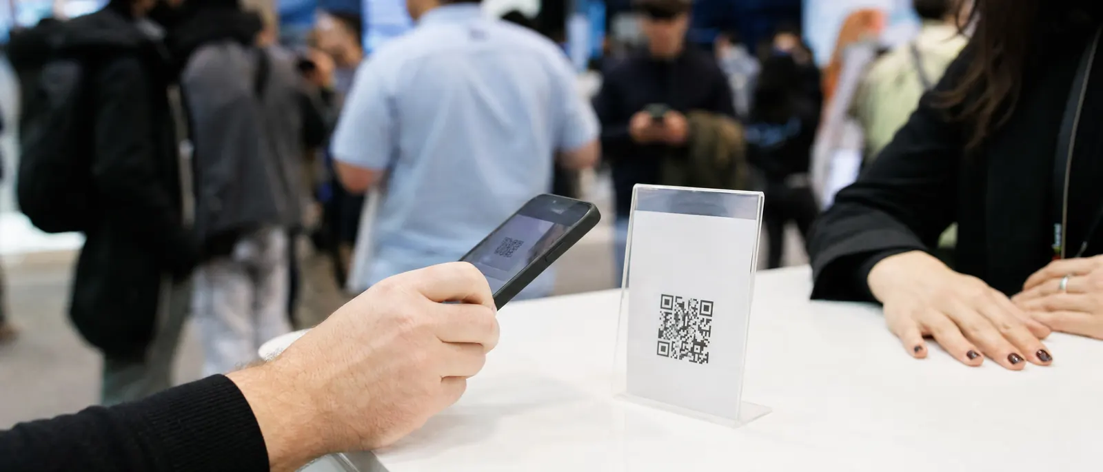 A visitor at an exhibition stand scanning a QR code on an acrylic table card with their phone